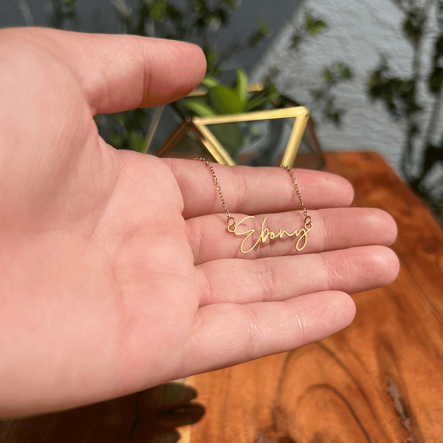 A hand holding a gold necklace with the name "Ebony" engraved on it.