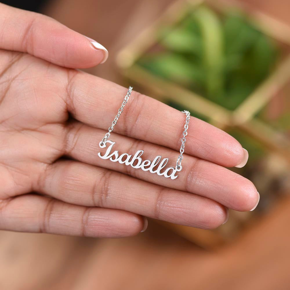 A hand holding a necklace with the name "Isabella" engraved on it.