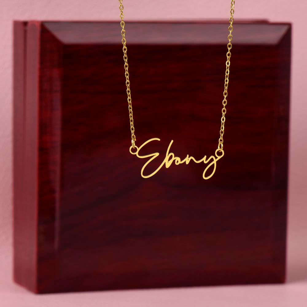 A gold necklace with the name "Ebony" engraved on a wooden box.